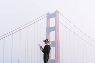 Golden Gate Köprüsü yakınlarındaki sis ve test cihazları sırasında VR gözlük takan isimsiz bir kadının tablete not aldığı yan görünüm