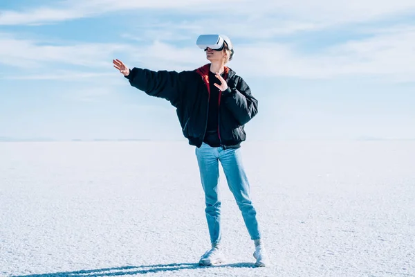 Full body of female tourist in outwear playing video game with virtual reality glasses while having tour in Bonneville Salt Flats in USA