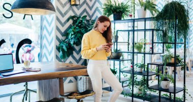 Kızıl saçlı milenyum blogcusu gündelik giysiler içinde tavan arası tasarımı içinde duruyor ve cep telefonuyla mesajlaşma sırasında mesaj göndermek için SMS yazıyor, çekici hippi kız e-posta yazıyor.