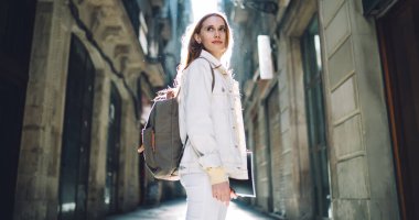 Barcelona 'daki eski binalar arasında kitap ve sırt çantası olan çekici ve zeki bir kadının yan görünüşü