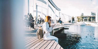 Kızıl saçlı bayan turist cep telefonu aygıtını kullanarak 4G kablosuz bağlantısını kullanarak milenyumlar için seyahat sitesinde geziniyor ve blog yazıyor.