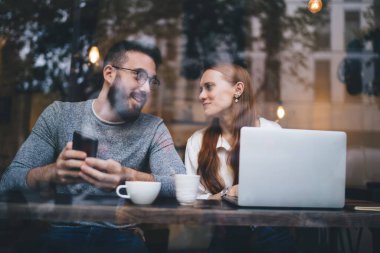 Modern kafedeki masada dinlenen genç ve mutlu bir çift. Bu arada dizüstü bilgisayar ve akıllı telefon kullanıyorlar ve ara verdiğimizde birbirlerine bakıyorlar.