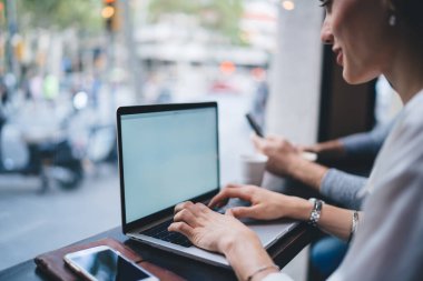Cep telefonuyla internette sörf yapan ve güneşli bir günde boş ekranla netbook 'ta yazan neşeli kadın çalışanın ekili görüntüsü.