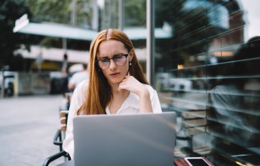 Pencerenin yanındaki kafede oturan ve gündüzleri iş projesinde çalışırken dizüstü bilgisayar kullanan kadın gözlüklü konsantre bir serbest çalışan.