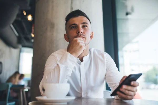 Pensive Muž Sedí Stolu Mobilním Telefonem Zamyšleně Odvrací Pohled Zatímco — Stock fotografie