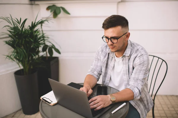 穿着休闲装和眼镜的男性聚精会神地坐在圆桌边浏览笔记本电脑 同时在创造性的工作空间中工作 — 图库照片