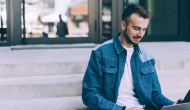 Gülümseyen beyaz adam blogcu modern teknoloji paylaşımı yayınını kullanıyor ve iletişim kuruyor, Webinar 'ı izleyen zeki genç hippi öğrenci dışarıda dizüstü bilgisayarla ders alıyor.