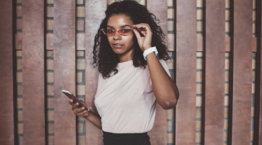 Sosyal ağlar iletişiminden memnun olan akıllı telefonda uygulama kullanan esmer, kıvırcık saçlı hippi kızın portresi. 20 'li yaşlarda Afro-Amerikan bir kadının cep telefonu etkisi altında olması.