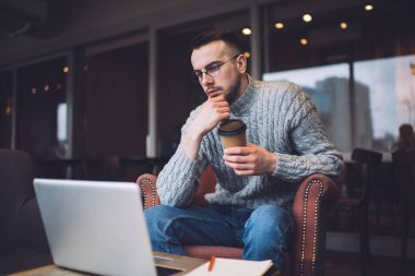 Restoranda dinlenirken, masa başında oturup ilginç günlük haberler okuyan, modaya uygun kıyafetler giyen serbest çalışan bir erkek.