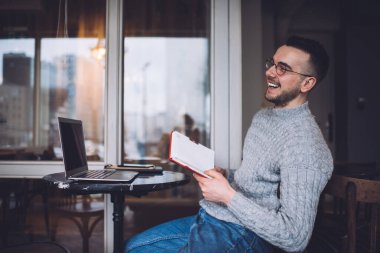 Serbest giyinen, serbest giyinmiş, elinde netbook ile masada oturan ve uzaktan çalışan genç bir erkek.