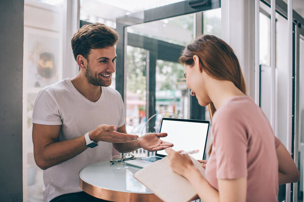 Спортивный молодой мужчина разговаривает с улыбчивой женщиной, делая заметки о стратегии будущей работы в кафе при солнечном свете