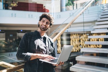 Ellerinde modern ağ kitabıyla neşeli bir Türk yazılım geliştiricisi içeride duruyor ve gülüyor, mutlu bir Orta Doğulu küçük sahibi teslimat bültenini bekliyor. Laptop bilgisayarını tarama için kullanıyor.