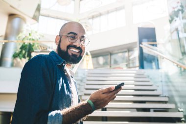 Kameraya gülümseyen, modern akıllı telefon cihazı takan, gözlüklü, başarılı bir erkek, kameraya gülümseyen klasik görüş koruması için klasik gözlüklü neşeli işadamının yarım boy portresi.