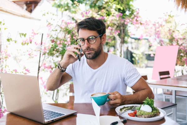 Kapuçino Içerken Cep Telefonuyla Konuşan Konsantre Bir Erkek Tost Yerken — Stok fotoğraf