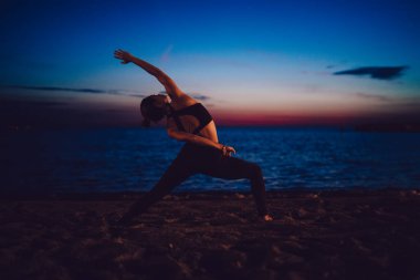 Akşamları deniz kıyısında hatha antrenmanı yapan esnek kadın yogi vücut kaslarını esneterek mükemmel incecik vücut hatlarını koruyor. Kıyı şeridindeki pilates eğitimi sırasında doğadan ilham alan sağlıklı bir kız.