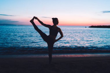 Akşamları deniz kıyısında hatha antrenmanı yapan esnek kadın yogi vücut kaslarını esneterek mükemmel incecik vücut hatlarını koruyor. Kıyı şeridindeki pilates eğitimi sırasında doğadan ilham alan sağlıklı bir kız.