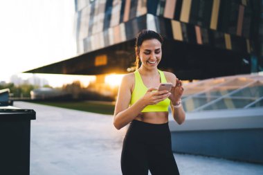 Gülümseyen beyaz kadın koşucu idman sonuçları hakkında tebligat okuyor zayıf, zengin kadın spor blogcusu açık hava antremanından sonra web sitesinde geziniyor.