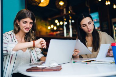 Modern kafeteryadaki yuvarlak masada birlikte oturan ve yeni başlatılan projelerde alet ve defter kullanan gündelik kıyafetli genç ve zeki kadınlar.