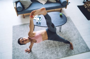 Tüm vücudun altından, çıplak ayaklı genç kadın modern odada utthita vasissthssana pozisyonu yaparken etkin olarak esnek bacaklar giyer.