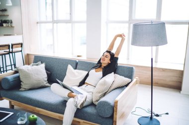 Rahat oturma odasında dizüstü bilgisayar üzerinde çalıştıktan sonra gündelik giysiler içinde genç bir kadının yüksek açılı koltukta oturup dinlenmesi.