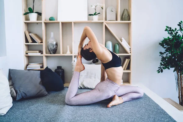希德在舒适的公寓里看到身穿运动服的身材纤细的无名女子在地板上练习瑜伽 还做了一只腿的王鸽 Asana — 图库照片