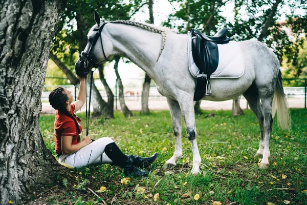 Gute Jockeyspielerin Zwanzigerin Sitzt Auf Gras Neben Baum Und Kümmert — Stockfoto