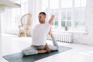 Marka adı ya da marka adı için tişörtü olan yakışıklı bir adam. Evde yoga yapıyor. Asana 'da nefes alıp veren ve sağlıklı bir yaşam tarzı için vücudunu esneten sakin bir erkek.