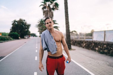 Eğitimden sonra caddede ayakta duran yakışıklı beyaz erkek sporcunun yarım boy portresi. Zayıf sporcu kameraya bakıyor ve sağlıklı aktif yaşam tarzını koruyor.