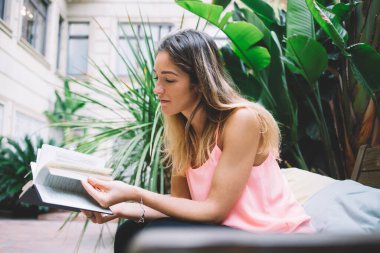 Tahta bankta oturan ve terasta vakit geçirirken ilginç kitaplar okuyan pozitif kadın.