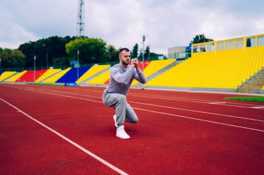 Aktif giyinmiş, sabahları bacaklarına çömelme egzersizleri yapan, spor kıyafetli, antrenmanlara ve stadyumda kalori kaybetmeye zaman harcayan beyaz erkek.