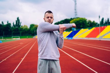 Aktif haldeki yakışıklı erkek portresi vücut kaslarını esnetiyor, kardiyodan önce egzersiz yapıyor, ciddi kararlı hippi adam sağlıklı yaşam tarzını koruyor eğitimden sonra sağlığına ve canlılığına kavuşuyor.