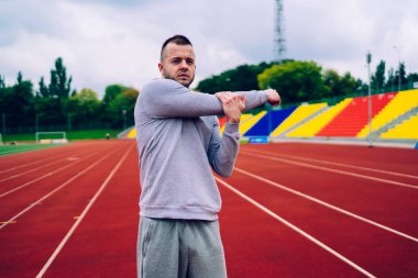 Aktif görevde olan güçlü genç sporcu stadyumda dikilirken kameraya bakıyor ve sıkı antrenmandan sonra pazılarını esnetiyordu.