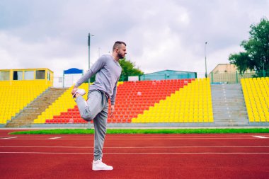 Aktif giyimli, sabah egzersizi yapan ve koşu için bacaklarını esneten 20 'li yaşlarda, dalgın erkek koşucu vücudunun alt kısmı için egzersiz yapıyor sağlıklı yaşam tarzını koruyor ve zindeliğe ulaşıyor.