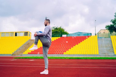 Tüm vücudun düşük açısı eşofman ve spor ayakkabı giyen koşucu bulutlu gökyüzüne karşı boş stadyum yolunda tek başına koşuyor.