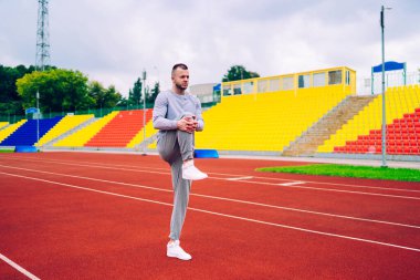 Eşofman giyen, alt vücut kaslarını esneten, zindelik ve zindelik için sabah antrenmanı yapan, sağlıklı yaşam tarzını koruyan, zayıflama için sabah antrenmanı yapan ciddi beyaz bir adam.