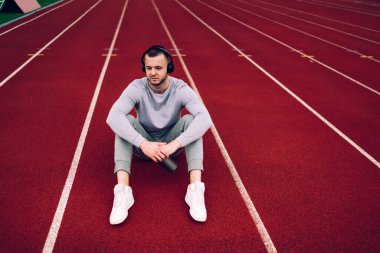 Aktif görevde olan yakışıklı beyaz erkek sporcu, antrenmandan sonra dinleniyor kulaklıkla favori şarkı listesinin sesini dinliyor, dalgın hipster koşucusu stadyumda müzik dinliyor.