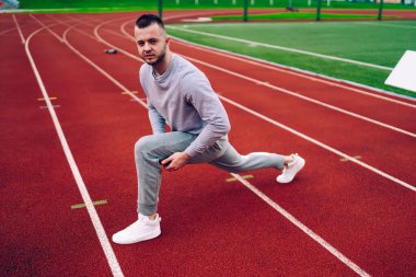 Aktif giyimli ve spor ayakkabılı kararlı erkek sporculardan bacak egzersizleri yaparken yarış pistinde egzersiz yapanlardan.