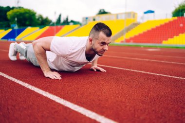 Aktif giyimli ve spor ayakkabılı güçlü sporcunun antrenmana hazırlanırken yarış pistinde yaptığı itme egzersizlerin yan görüntüsü