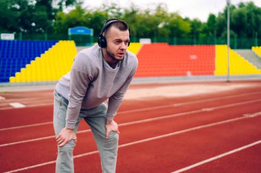 Stadyumda antrenman yaptıktan sonra spor giyinen ve yarış pistinde durup kulaklıkla müzik dinleyen ciddi etnik sporcu.