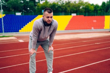 Stadyumda dinlendikten sonra nefes alan yorgun, yorgun, beyaz erkek koşucu spor yaptıktan sonra yorgun ve sağlıklı yaşam tarzı hedeflerine ulaşan ciddi kararlı koşucu.
