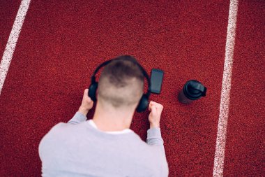 Kafkasyalı bir erkek akıllı telefona bağlı kulaklıkla müzik dinliyor. Genç bir hipsterın esneme hareketleri ve esneklik eğitimi alıyor. Cep telefonu şarkılarından keyif alıyor.