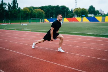 Siyah eşofmanlı kararlı beyaz adam antrenman için çömelme, vücut ısıtma, vücut geliştirme, vücut geliştirme esnekliği ve stadyum antrenmanında fiziksel güç.
