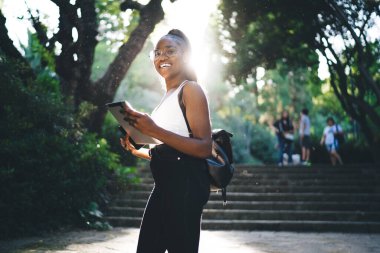 Basamakların yanında durup tablet tutan, günlük giysiler ve gözlüklerle çekici, şık, genç bir Afro-Amerikan kadın.