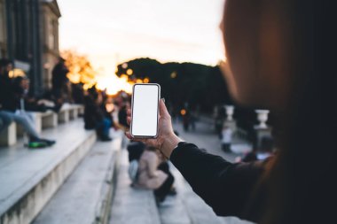 Sokakta gün batımına karşı dururken günlük kıyafetleriyle selfie çeken tanınmamış bir kadının arka plan görüntüsü.