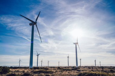 Yüksek voltajlı yel değirmenlerinin altından boş vadideki siluetler ince bulutlu mavi gökyüzüne karşı çevre dostu elektrik üretiyor.