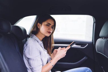 Somurtkan kadının yan görünüşü. Günlük giysiler içinde arabanın arka koltuğunda oturan ve gündüz vakti araba camına bakan kadın.