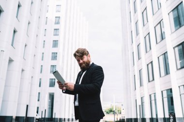 Tabletteki iş görüşmesi sırasında gökdelenlerin yanındaki patikada dururken gülümseyen ve kameraya bakan başarılı ofis çalışanı.