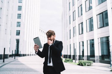 Şık giyinmiş düşünceli bir erkek, ağzı kapalı, elleri sokakta duruyor ve yeni iş projesiyle ilgili internette geziniyor.