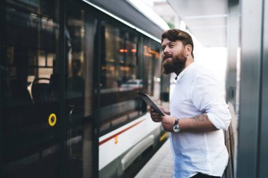 Tablet ve kol saati olan sakallı bir erkek çalışanın modern şehirde durmayı bekleyen beyaz gömlekli hali.