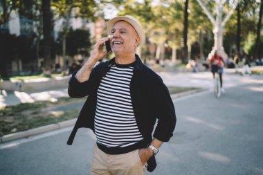 50 yaşında neşeli bir erkek, gündüzleri gülerken, cep telefonuyla konuşuyor.